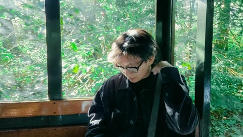 Kwanho looking down beside a green window